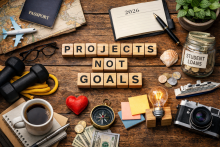 Flat-lay photograph symbolizing “projects over goals,” featuring a notebook labeled 2026, travel items, fitness equipment, money, and creative tools arranged around the phrase “Projects Not Goals.”