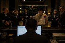 An overnight hotel agent checks in a flight crew while an injured guest with a bandaged shoulder waits nearby.